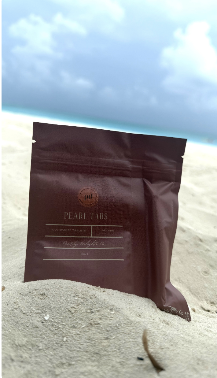 Pearly Delights Travel Kit — Pearl Tabs pouch and mini toothbrush on a sunlit beach table