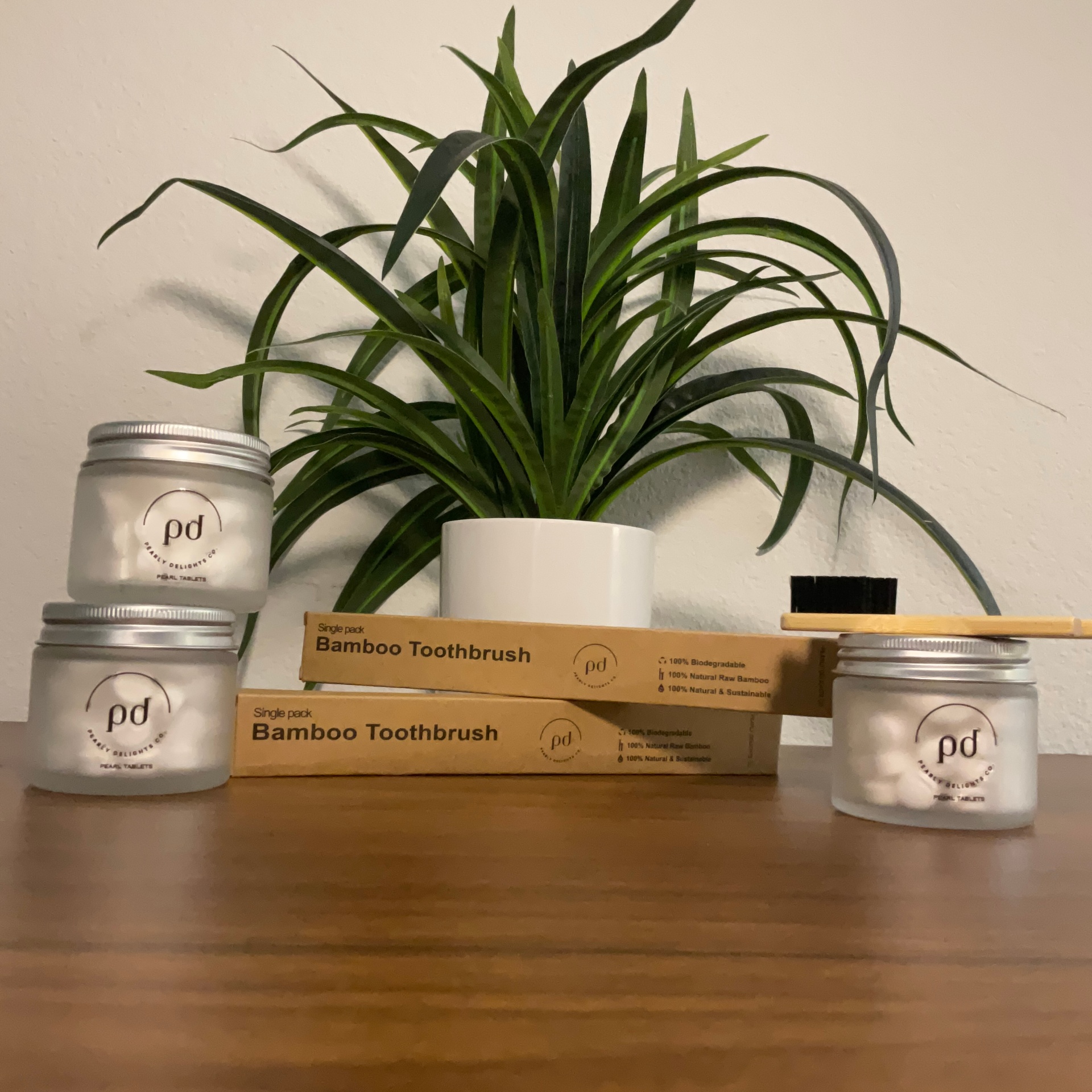 A jar of Pearly Delights toothpaste tablets, a blush toothbrush, and a terracotta travel pouch floating on a warm ivory background